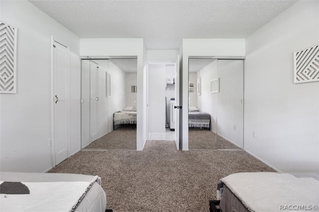 carpeted bedroom with a textured ceiling and multiple closets