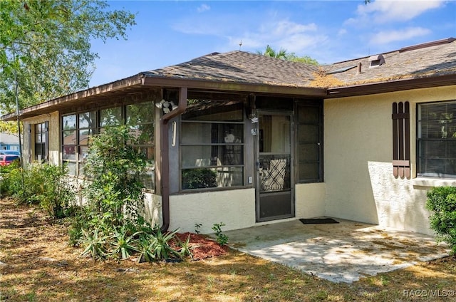 view of exterior entry with a shingled roof and stucco siding