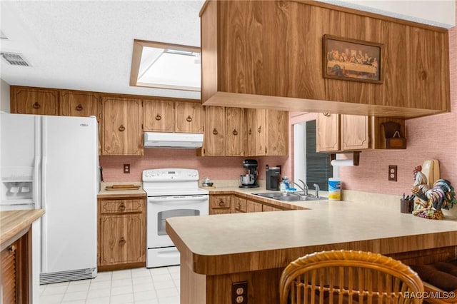 kitchen with a sink, white appliances, brown cabinetry, under cabinet range hood, and visible vents