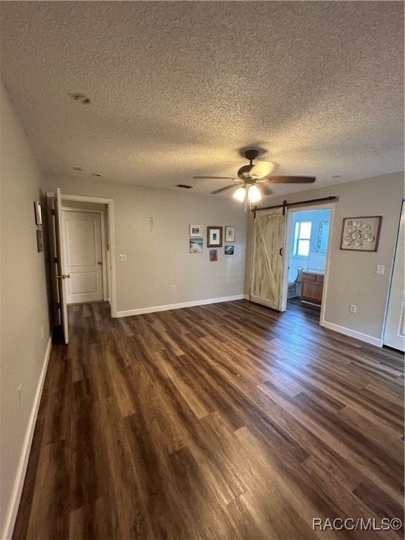 unfurnished room featuring a barn door, ceiling fan, dark hardwood / wood-style flooring, and a textured ceiling