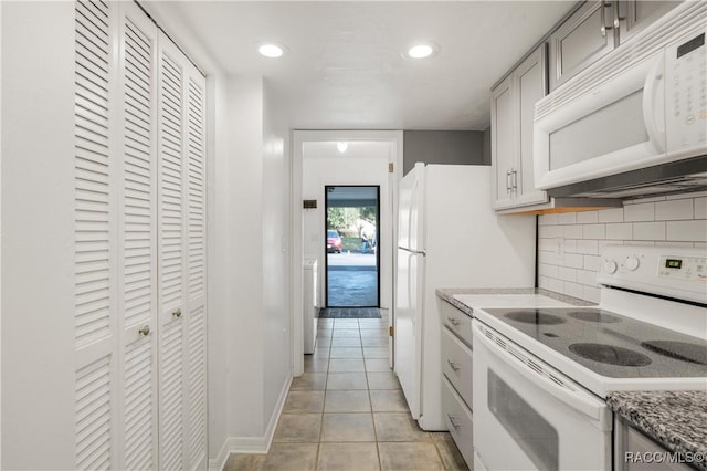 kitchen with light tile patterned flooring, white appliances, light stone counters, and backsplash