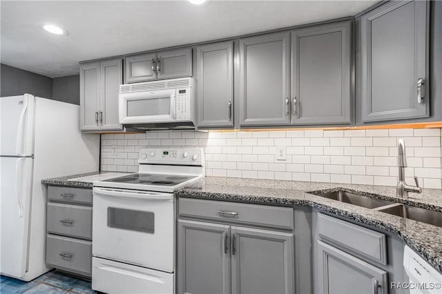 kitchen with gray cabinetry, dark stone countertops, white appliances, and sink