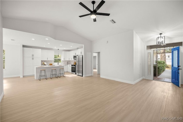 unfurnished living room with ceiling fan with notable chandelier, high vaulted ceiling, and light hardwood / wood-style flooring