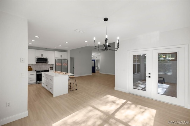 kitchen with white cabinetry, a center island, hanging light fixtures, appliances with stainless steel finishes, and light wood-type flooring