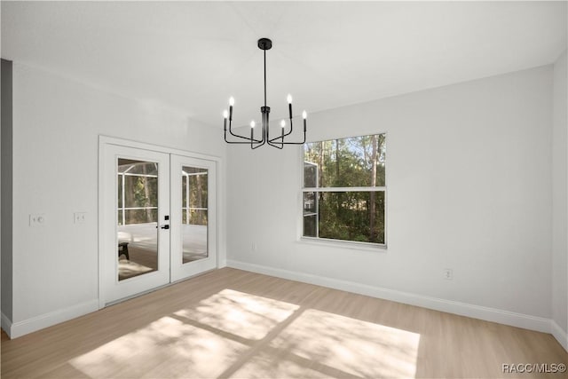 unfurnished dining area featuring french doors, a chandelier, and light wood-type flooring