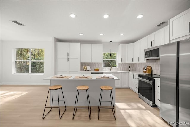 kitchen featuring a kitchen bar, tasteful backsplash, stainless steel appliances, white cabinets, and a center island