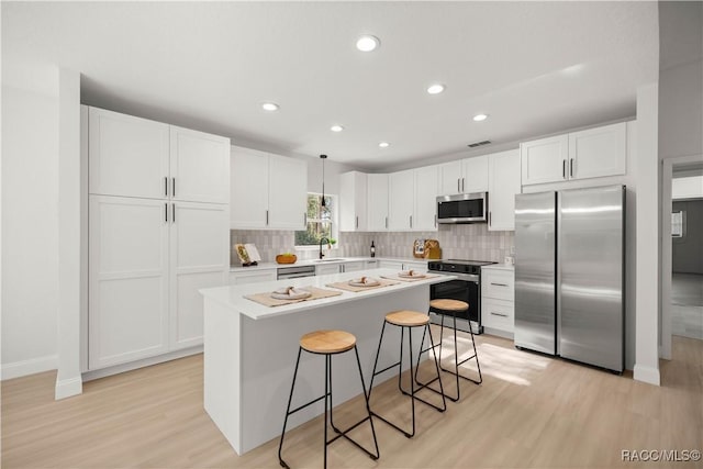 kitchen with a kitchen bar, light hardwood / wood-style flooring, pendant lighting, and appliances with stainless steel finishes