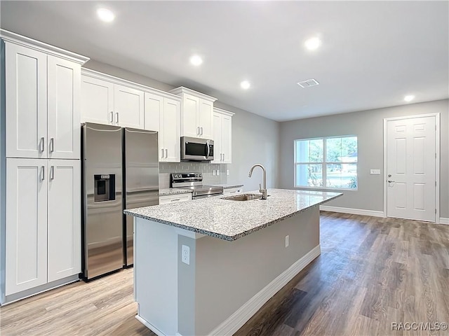 kitchen with appliances with stainless steel finishes, an island with sink, sink, white cabinets, and light stone countertops