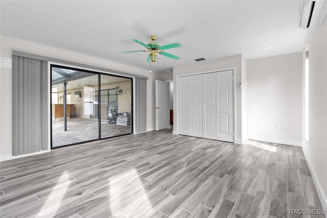 unfurnished bedroom featuring ceiling fan, access to exterior, a wall unit AC, and light hardwood / wood-style flooring