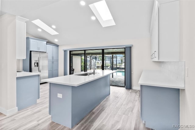 kitchen with a center island with sink, sink, vaulted ceiling with skylight, stainless steel fridge, and light hardwood / wood-style floors