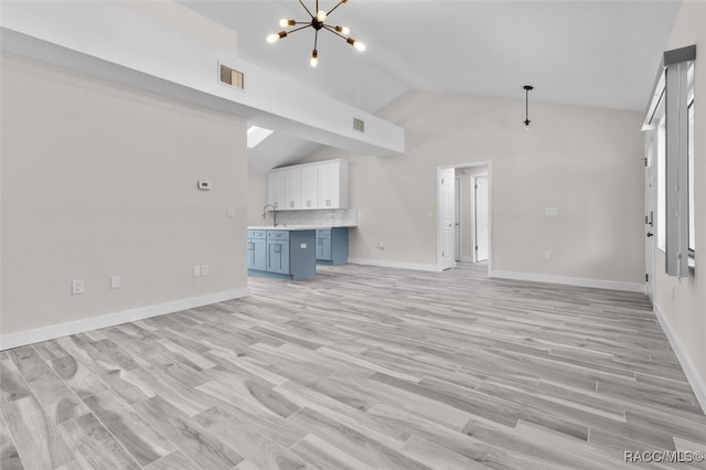 unfurnished living room with light hardwood / wood-style floors, lofted ceiling, sink, and a chandelier