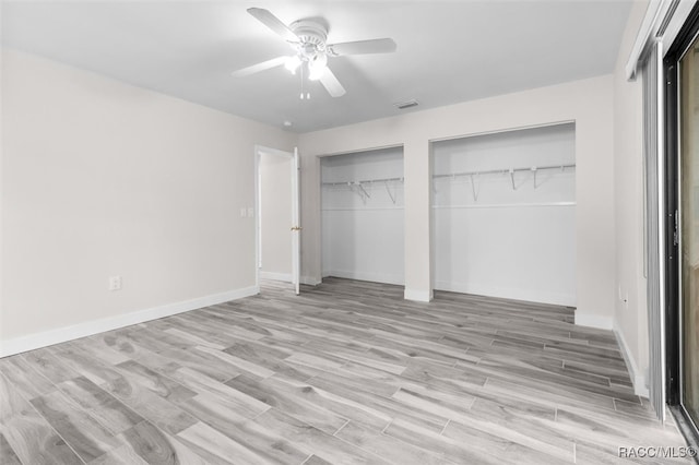 unfurnished bedroom featuring ceiling fan, light wood-type flooring, and multiple closets