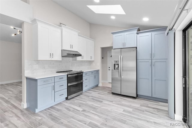 kitchen with white cabinetry, backsplash, lofted ceiling with skylight, light hardwood / wood-style floors, and appliances with stainless steel finishes