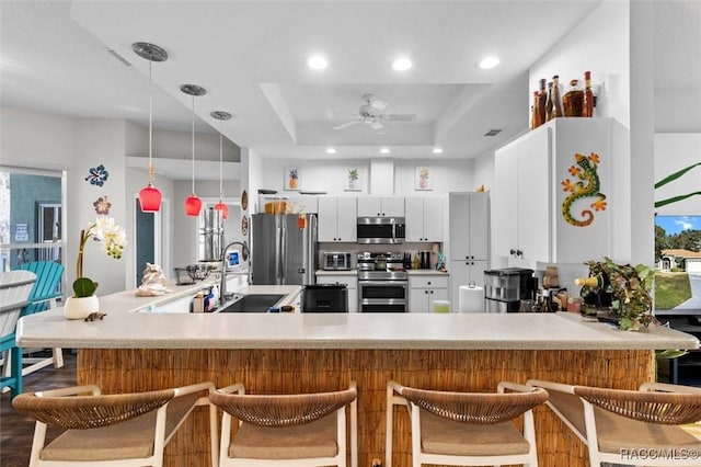 kitchen with appliances with stainless steel finishes, a raised ceiling, a sink, and a kitchen breakfast bar