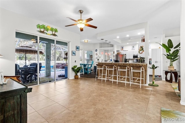 interior space featuring white cabinets, ceiling fan, a breakfast bar area, decorative light fixtures, and stainless steel appliances