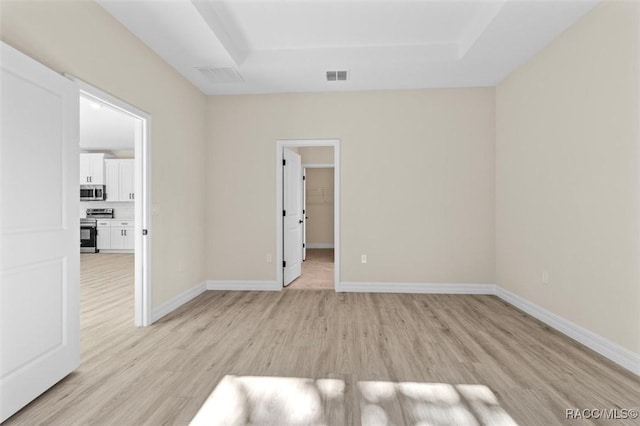 empty room with light wood-style flooring, visible vents, a tray ceiling, and baseboards