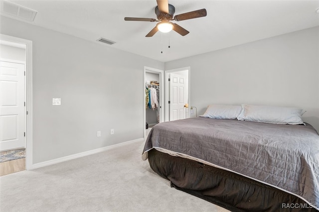 bedroom with a closet, a walk in closet, light colored carpet, and ceiling fan