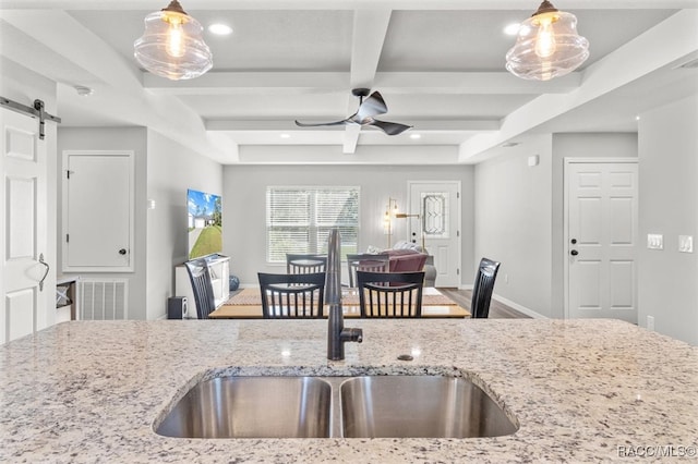 kitchen with light stone counters, sink, beam ceiling, a barn door, and hanging light fixtures