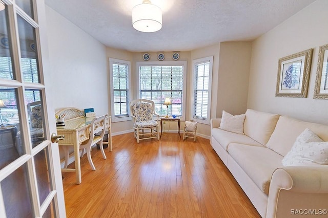 living room with a textured ceiling, light wood-style flooring, and baseboards