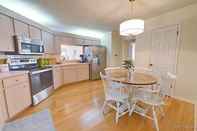 kitchen featuring light wood finished floors, light countertops, backsplash, appliances with stainless steel finishes, and light brown cabinets