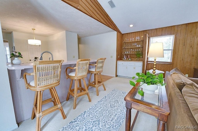 bar featuring visible vents, light colored carpet, wood walls, pendant lighting, and indoor wet bar