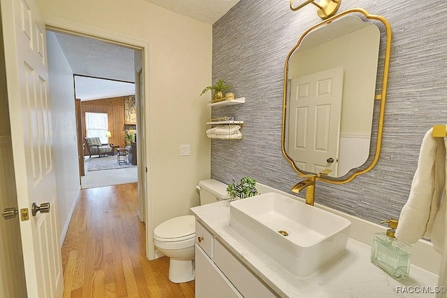 half bath with toilet, an accent wall, wood finished floors, and vanity