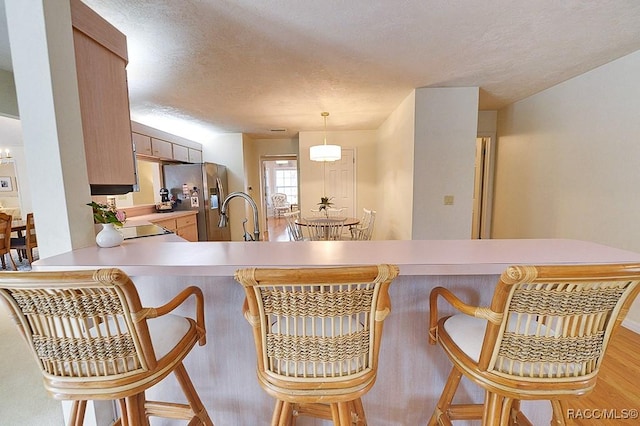 kitchen featuring light countertops, light wood-style floors, a sink, a textured ceiling, and stainless steel fridge with ice dispenser