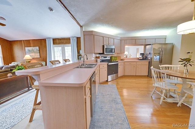 kitchen featuring appliances with stainless steel finishes, open floor plan, light brown cabinets, a sink, and a peninsula