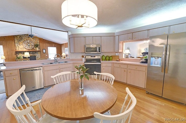 kitchen with vaulted ceiling, stainless steel appliances, light countertops, light wood-style floors, and a sink