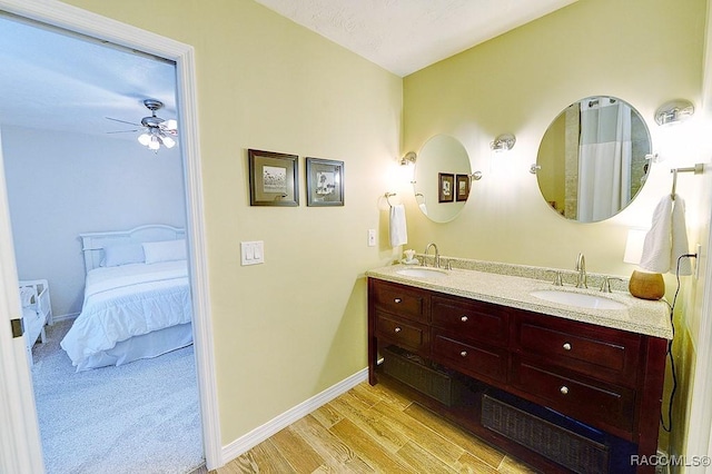 ensuite bathroom featuring wood finished floors, a sink, connected bathroom, and baseboards