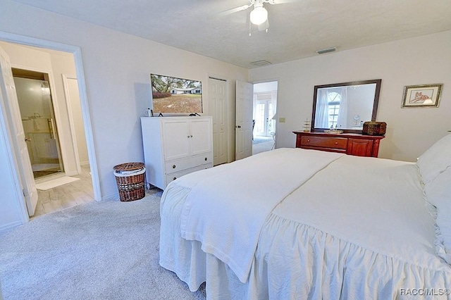 bedroom featuring light carpet, ensuite bath, visible vents, and a ceiling fan