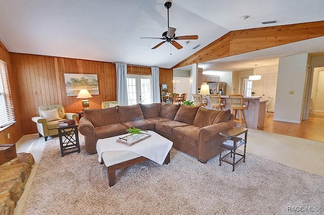 living room with lofted ceiling, visible vents, light wood-style flooring, wood walls, and ceiling fan