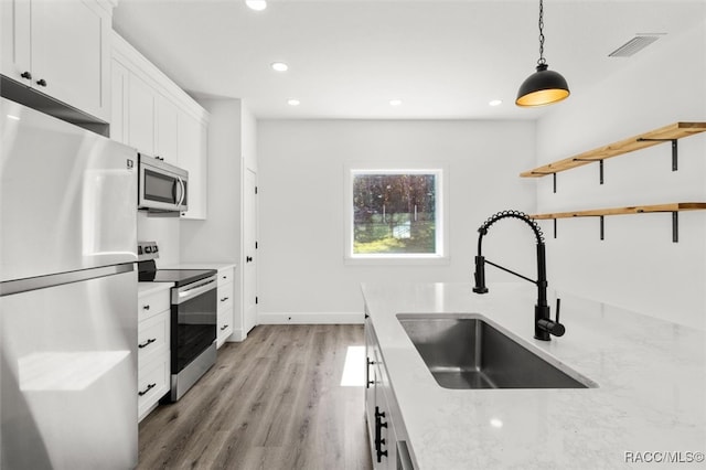 kitchen with white cabinets, sink, hanging light fixtures, light stone counters, and stainless steel appliances