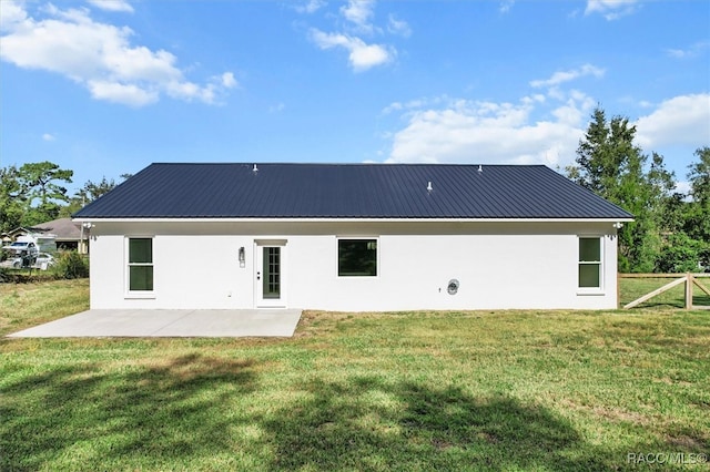 back of house featuring metal roof, a patio, a lawn, and stucco siding