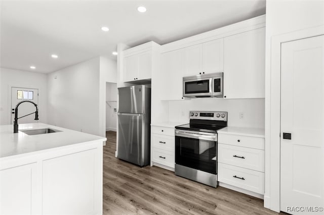 kitchen featuring stainless steel appliances, light countertops, light wood-style floors, white cabinetry, and a sink