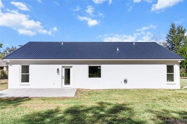 rear view of property with a yard, stucco siding, metal roof, and a patio