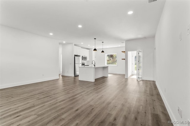 unfurnished living room featuring a sink, baseboards, wood finished floors, and recessed lighting