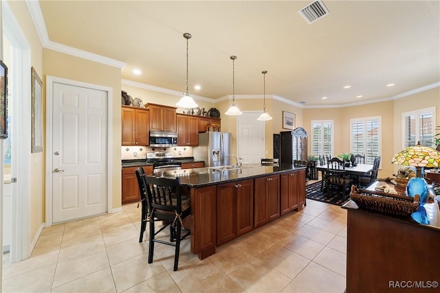 kitchen featuring a kitchen breakfast bar, appliances with stainless steel finishes, an island with sink, crown molding, and light tile patterned floors