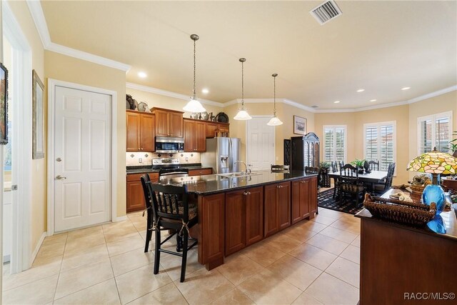 kitchen featuring a kitchen breakfast bar, appliances with stainless steel finishes, an island with sink, crown molding, and light tile patterned floors