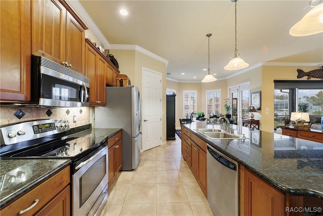 kitchen with sink, ornamental molding, an island with sink, hanging light fixtures, and appliances with stainless steel finishes