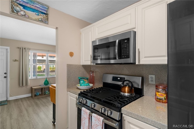 kitchen featuring decorative backsplash, appliances with stainless steel finishes, light hardwood / wood-style floors, and white cabinetry