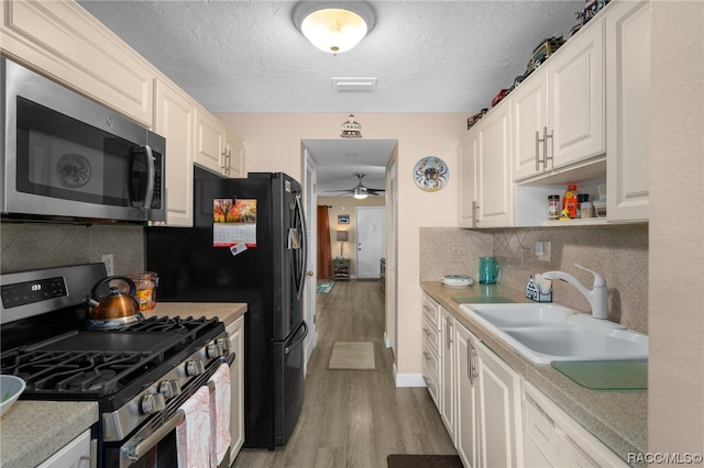 kitchen with backsplash, white cabinets, sink, light hardwood / wood-style flooring, and appliances with stainless steel finishes