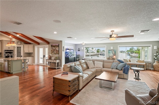 living room featuring vaulted ceiling with beams, ceiling fan, light hardwood / wood-style floors, and a textured ceiling