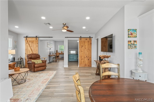 living room featuring a barn door, light hardwood / wood-style flooring, ceiling fan, and vaulted ceiling