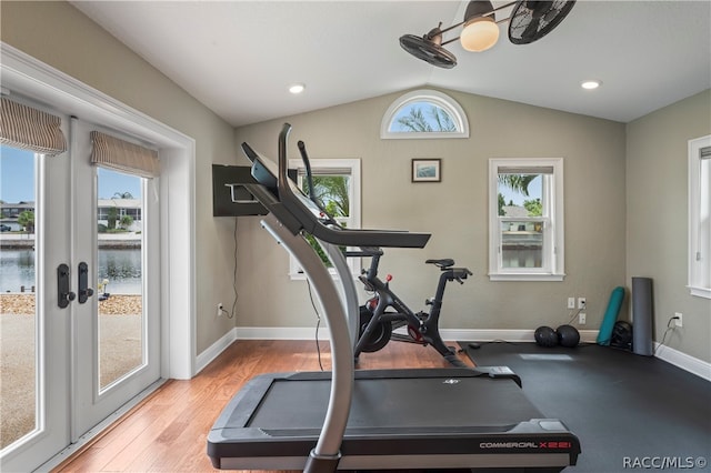 exercise room with plenty of natural light, a water view, light hardwood / wood-style floors, and lofted ceiling