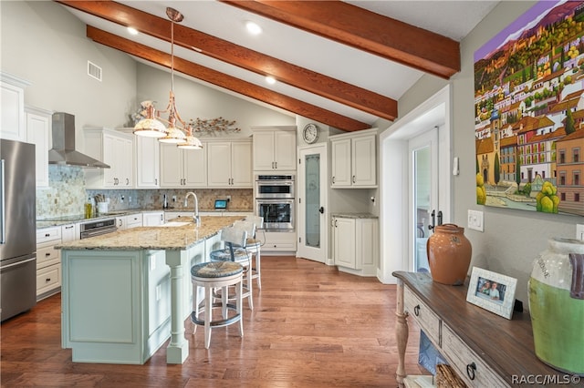 kitchen featuring a center island with sink, a kitchen breakfast bar, wall chimney range hood, light stone countertops, and stainless steel appliances