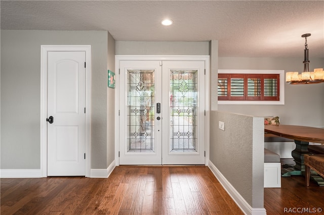 doorway to outside featuring an inviting chandelier, dark hardwood / wood-style flooring, a textured ceiling, and french doors