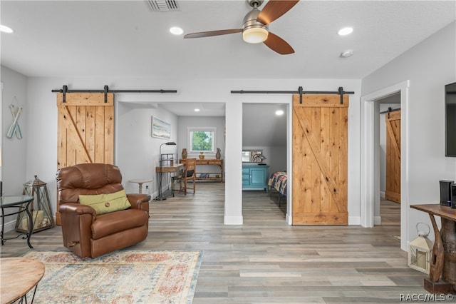 sitting room with a barn door, ceiling fan, and light hardwood / wood-style flooring