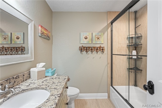 full bathroom with vanity, bath / shower combo with glass door, toilet, a textured ceiling, and wood-type flooring