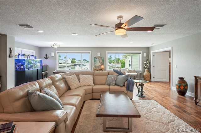 living room featuring ceiling fan, light hardwood / wood-style floors, and a textured ceiling